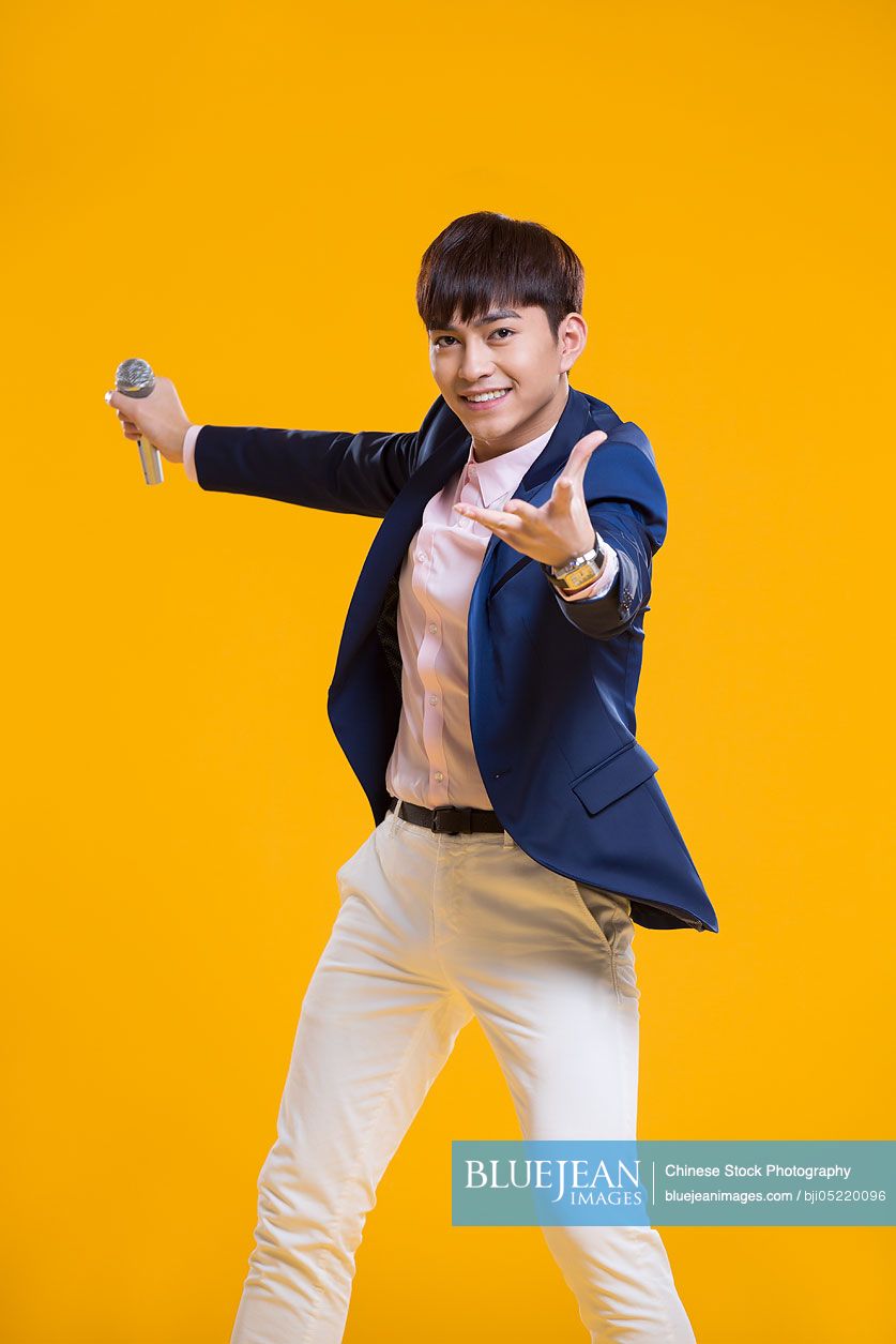 Cheerful young Chinese man singing with microphone