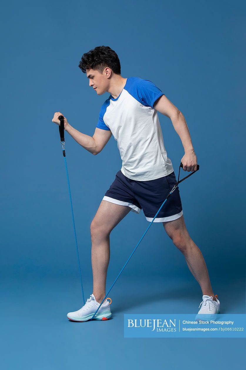 Studio shot of young Chinese man exercising with resistance band