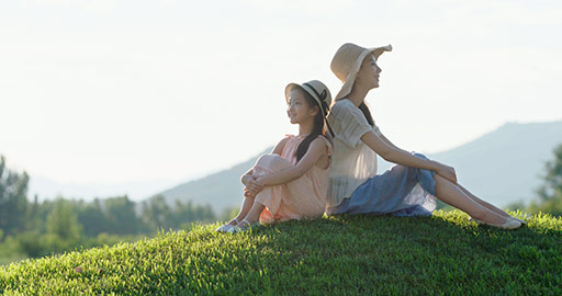 Happy Chinese mother and daughter sitting on meadow,4K