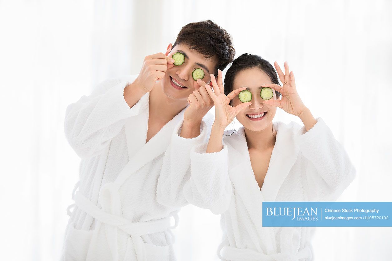 Young Chinese couple with cucumber slices on eyes