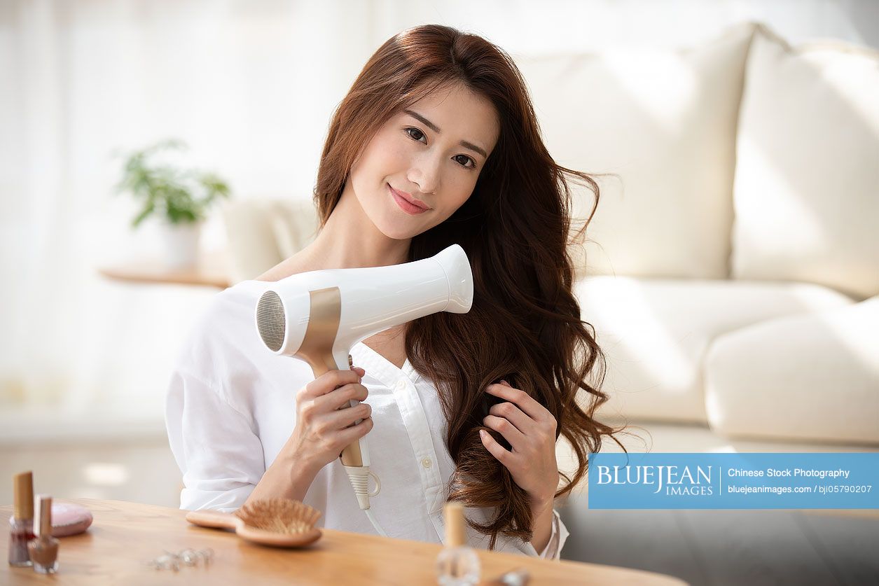 Young Chinese woman using hair dryer at home