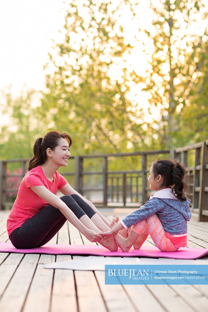 Happy Chinese mother and daughter doing yoga outdoors