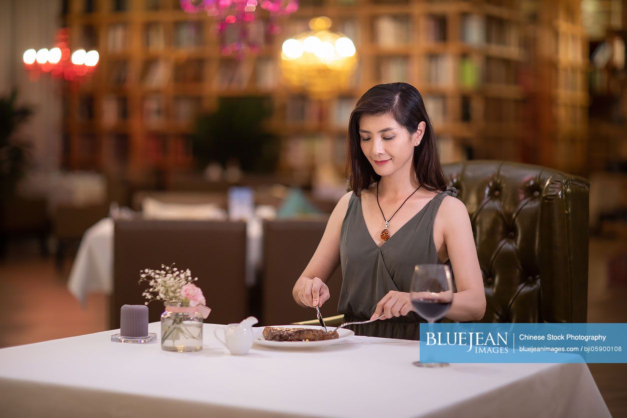 Elegant Chinese woman eating steak in western restaurant