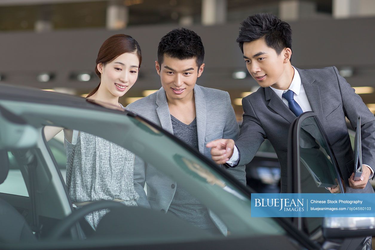 Young Chinese couple choosing car in showroom