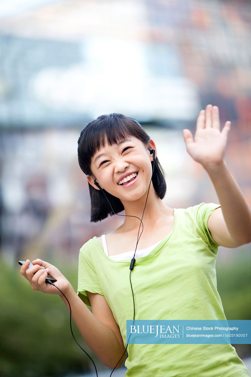 Happy Chinese schoolgirl listening to MP3 player and waving