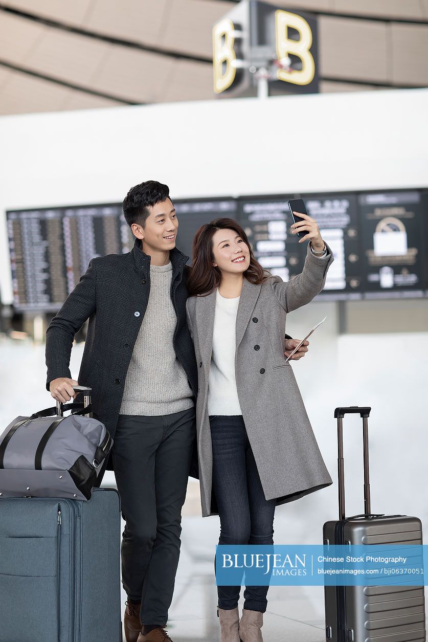 Happy young Chinese couple using smartphone at the airport