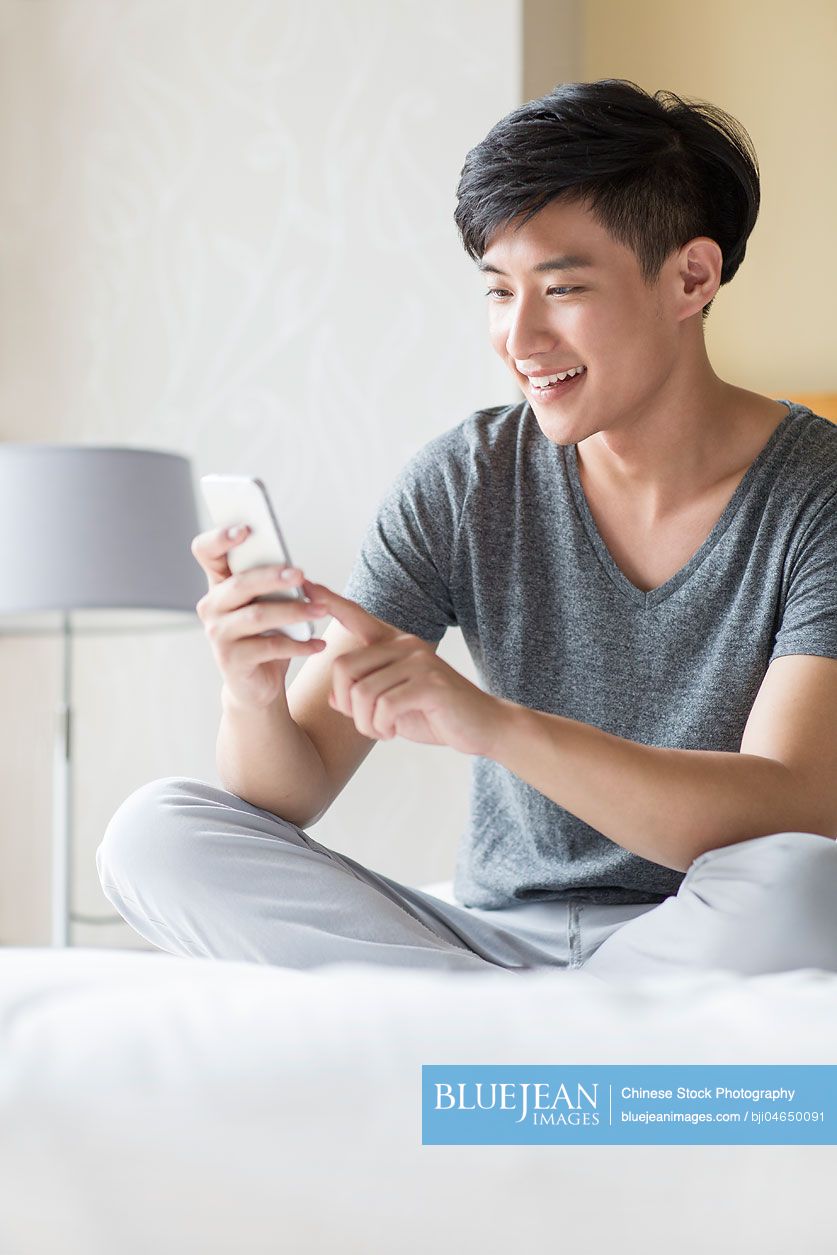 Young Chinese man using smart phone on bed