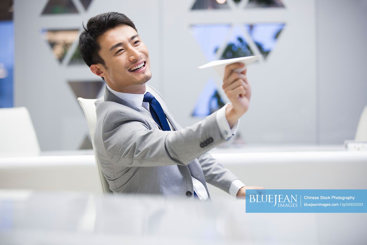 Young Chinese businessman flying a paper airplane