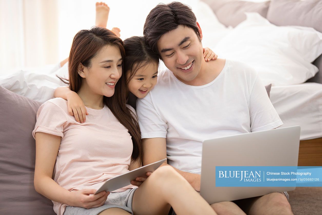 Happy young Chinese family relaxing in bedroom