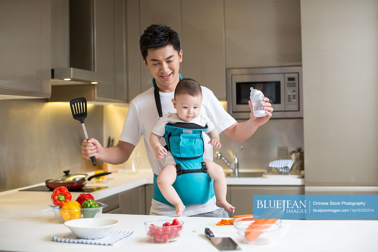 Chinese father holding baby and cooking in the kitchen