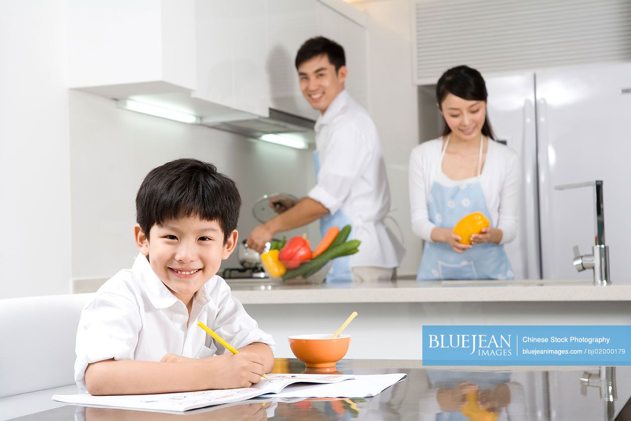 Chinese boy doing homework with parents in kitchen