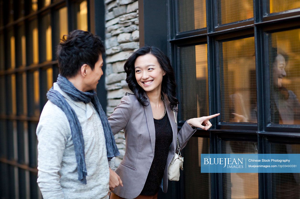 Sweet young Chinese couple doing window-shopping in city street