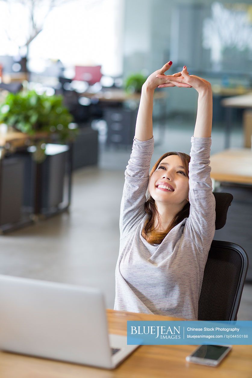 Young Chinese woman stretching in office