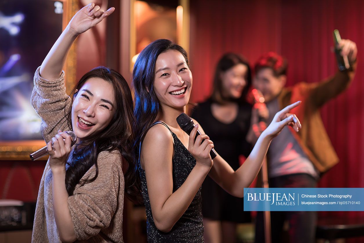 Happy Chinese friends singing karaoke in nightclub