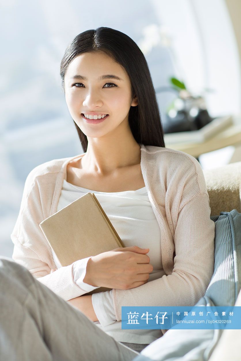 年轻女子拿着一本书坐在沙发上
