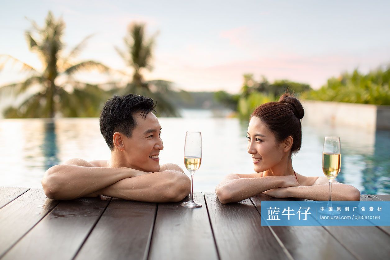 快乐的年轻情侣在泳池边喝香槟