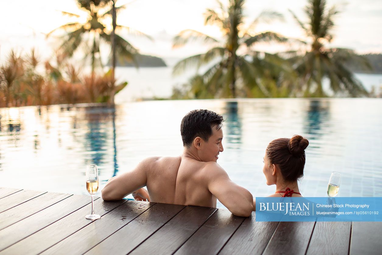 Happy young Chinese couple drinking champagne in swimming pool