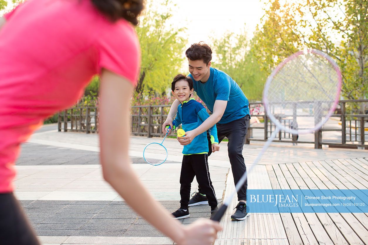 Happy young Chinese family playing badminton in park