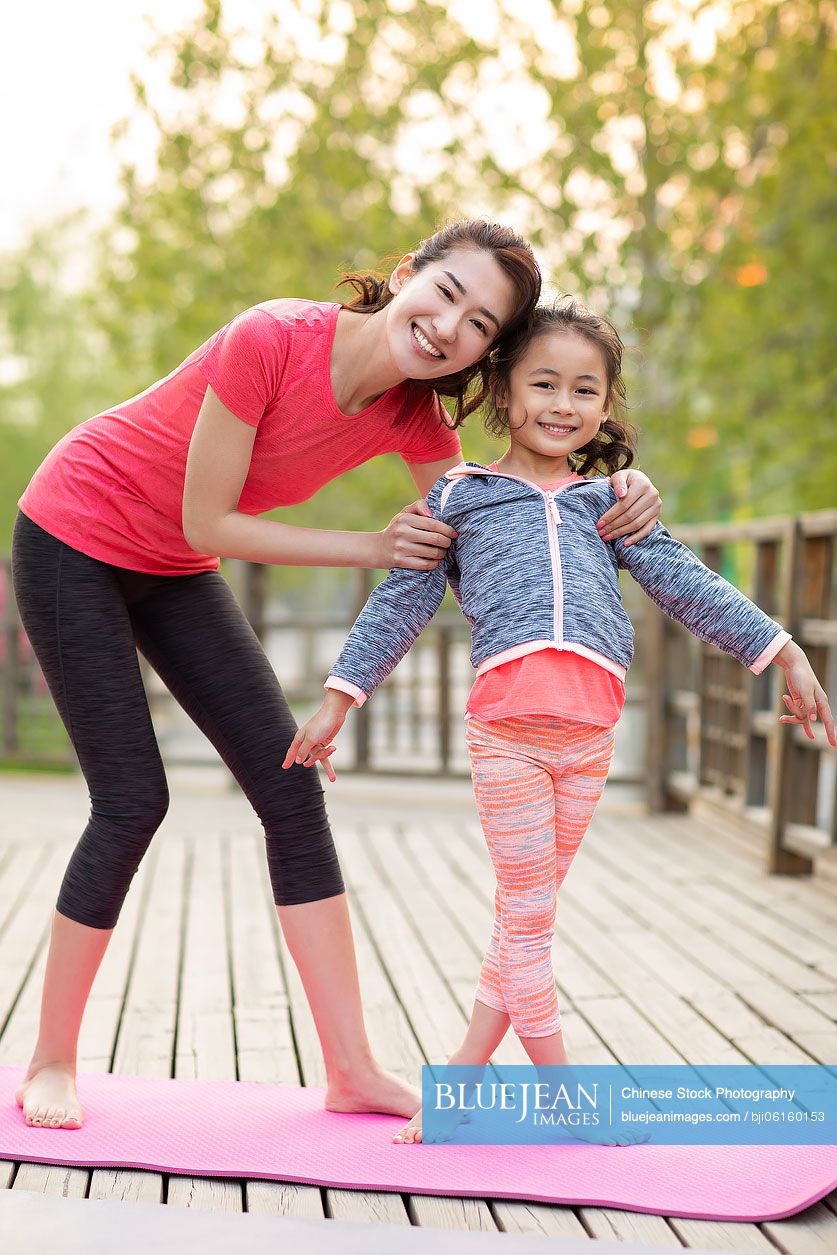 Happy Chinese mother and daughter doing yoga outdoors