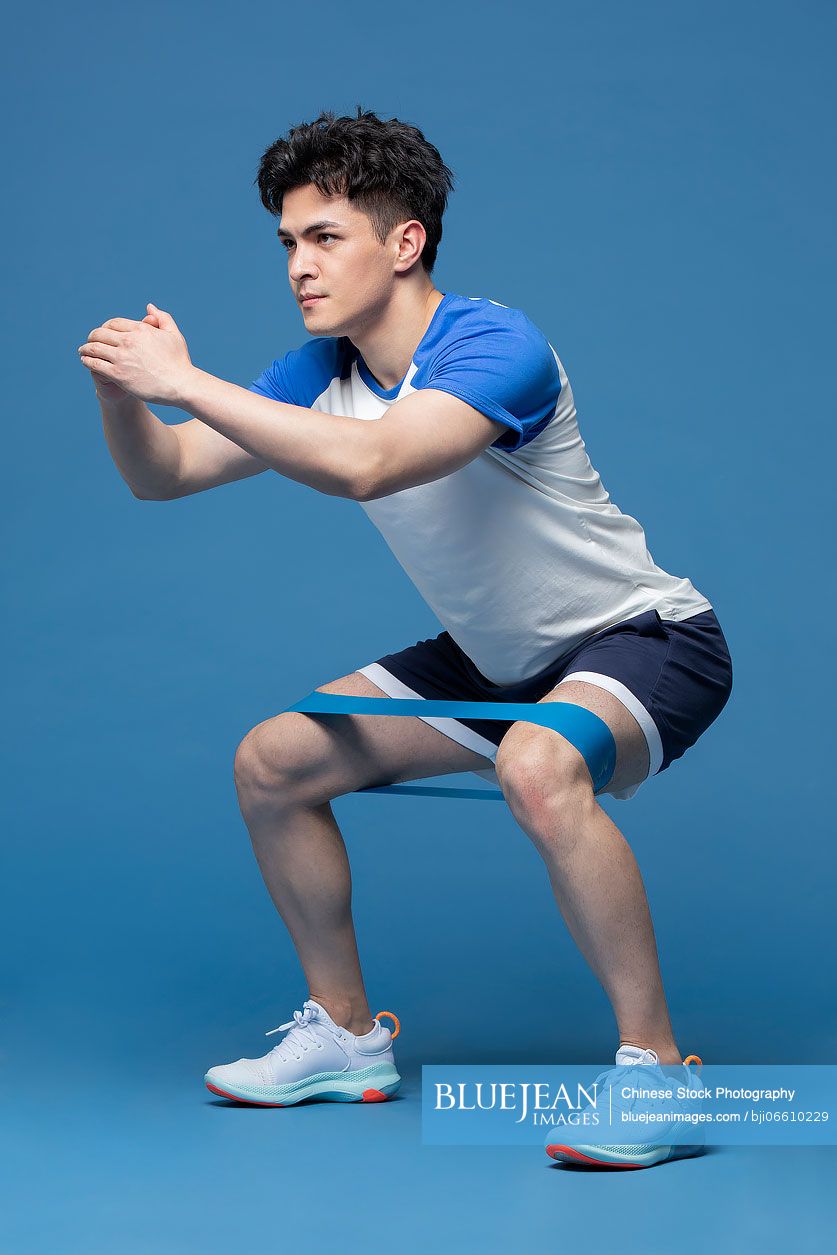 Studio shot of young Chinese man exercising with resistance band