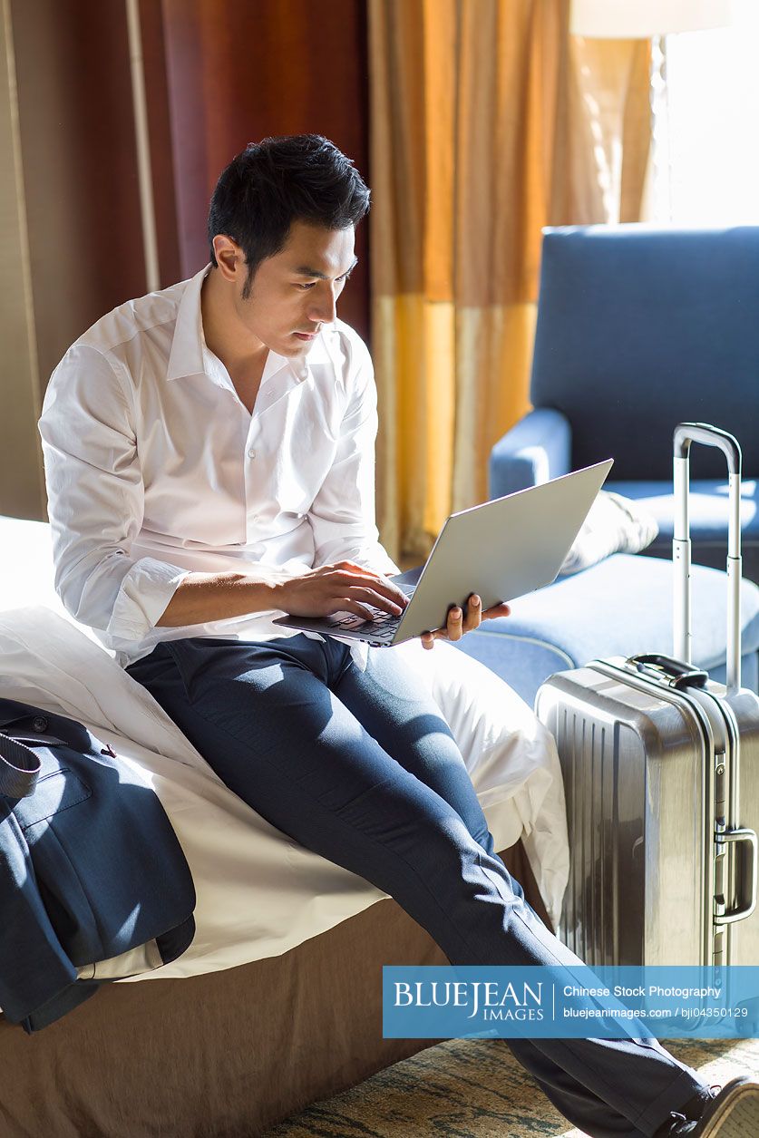 Young Chinese businessman using laptop in hotel room