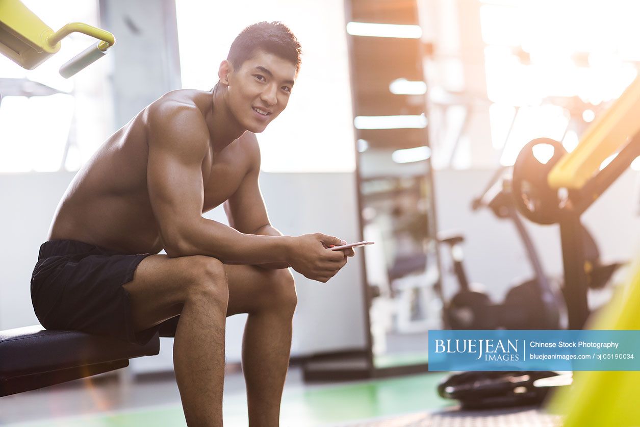 Young Chinese man using smart phone in gym