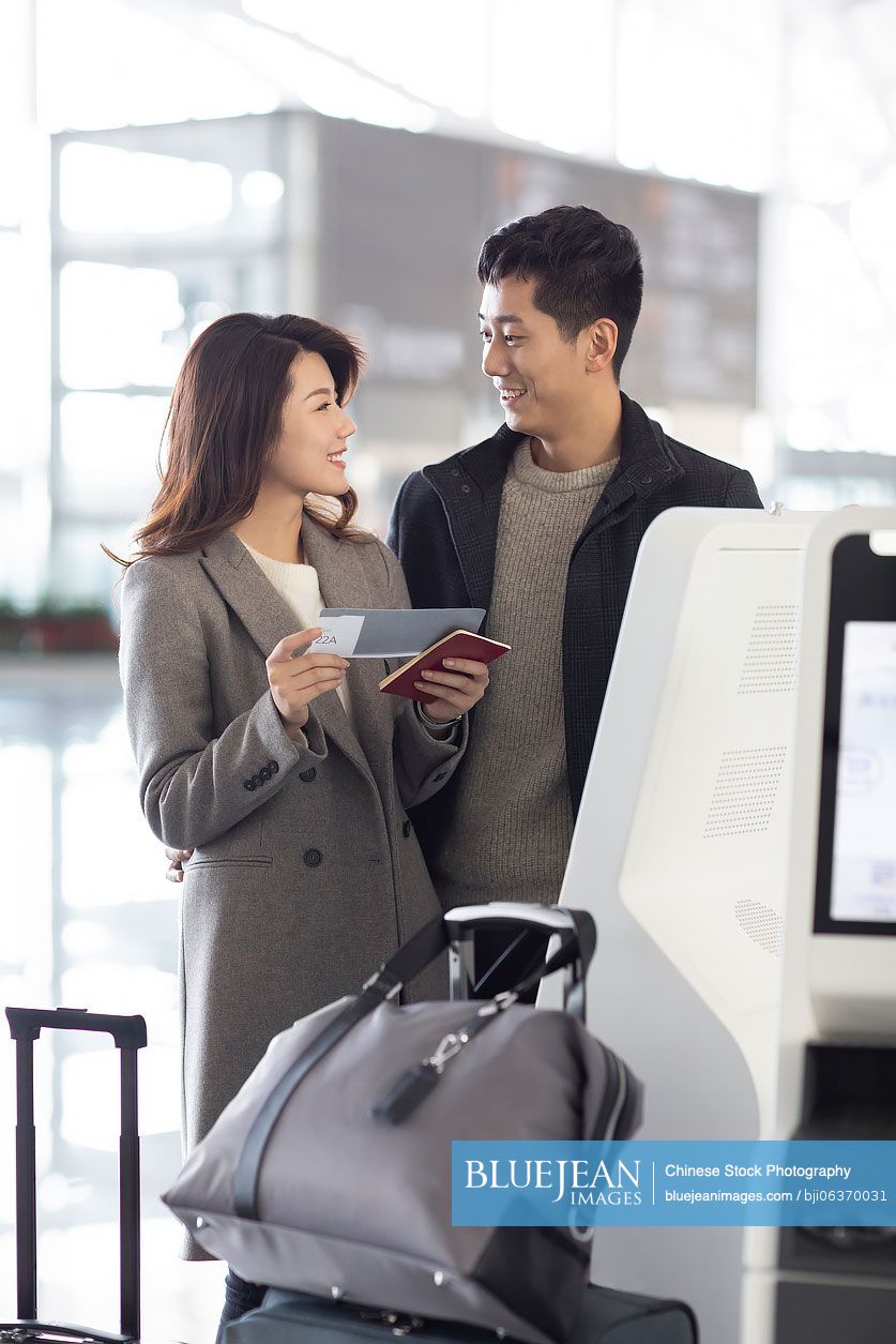 Happy young Chinese couple doing self check-in at the airport