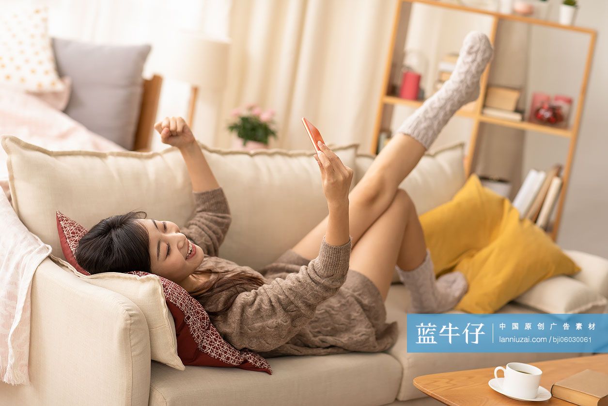 年轻女士躺在沙发上玩手机游戏