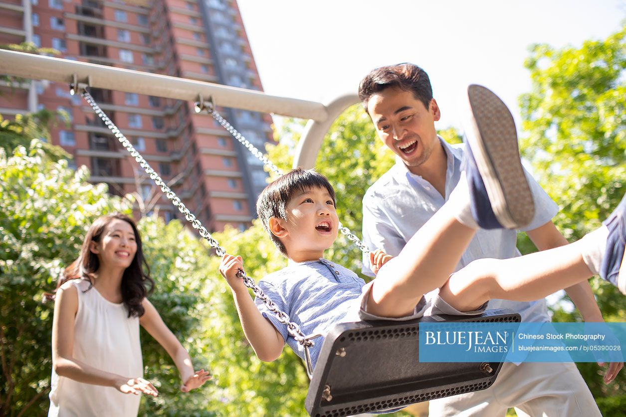 Happy young Chinese parents pushing son on swing