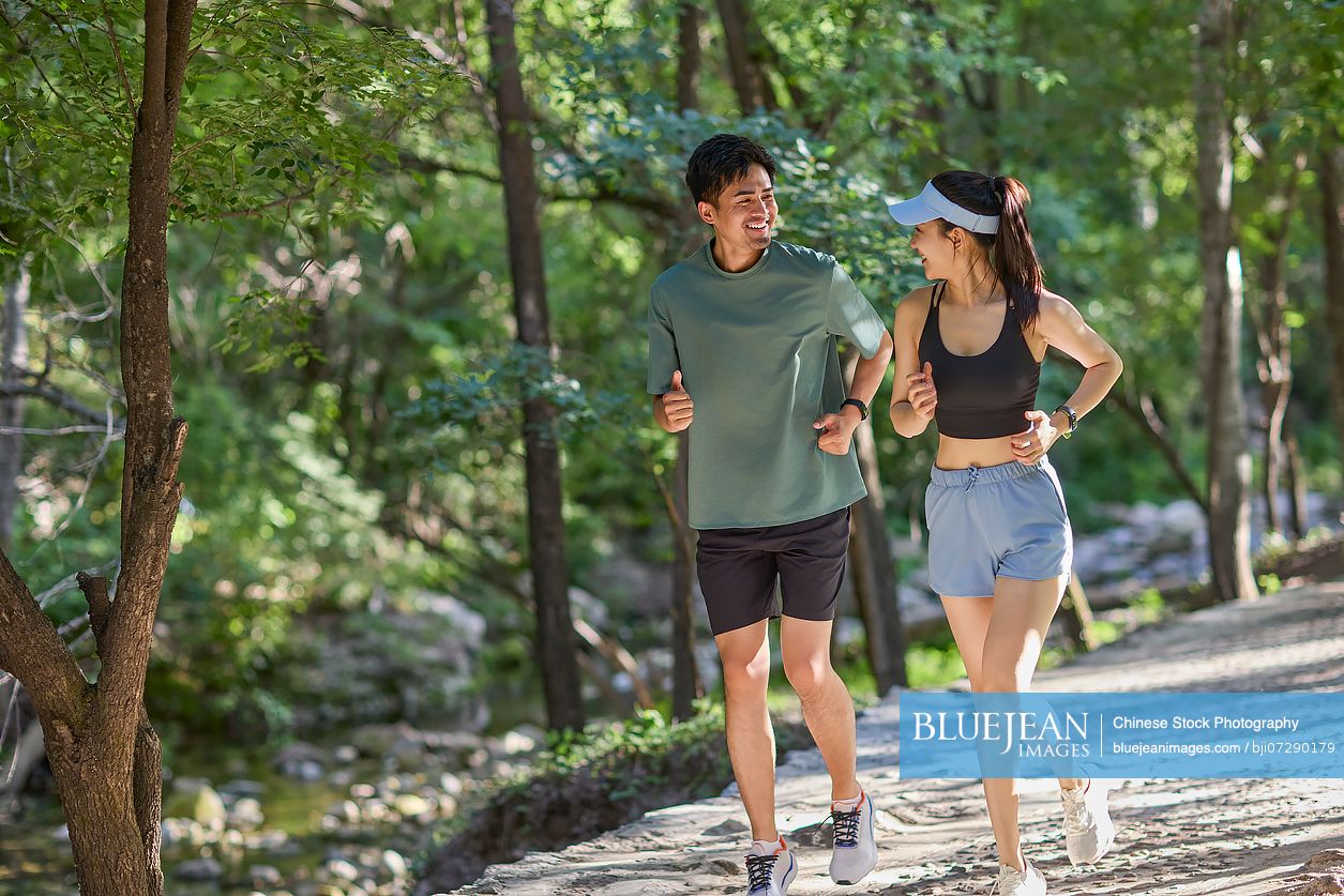 Young couple jogging along a path surrounded by lush trees