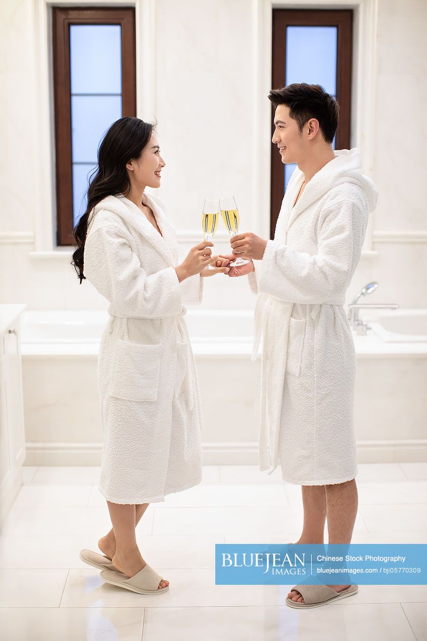 Happy young Chinese couple drinking champagne in bathroom