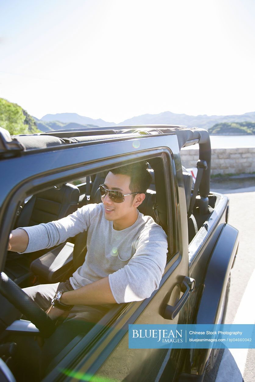 Happy young Chinese man driving a jeep