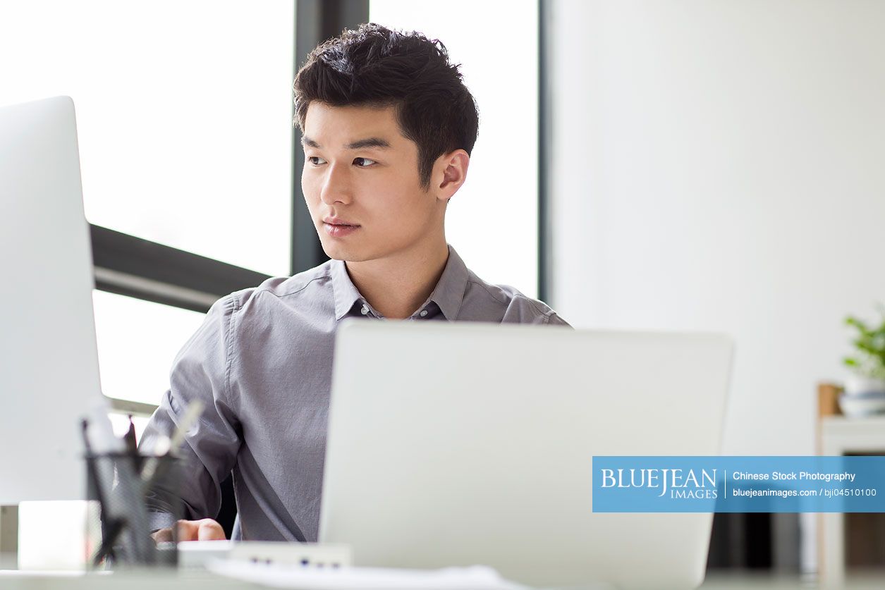 Young Chinese businessman using laptop in office