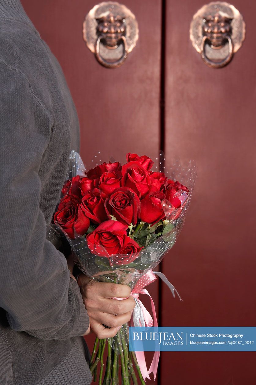 Chinese Young Man Waiting At Front Door With A Bunch Of Roses Behind His Back