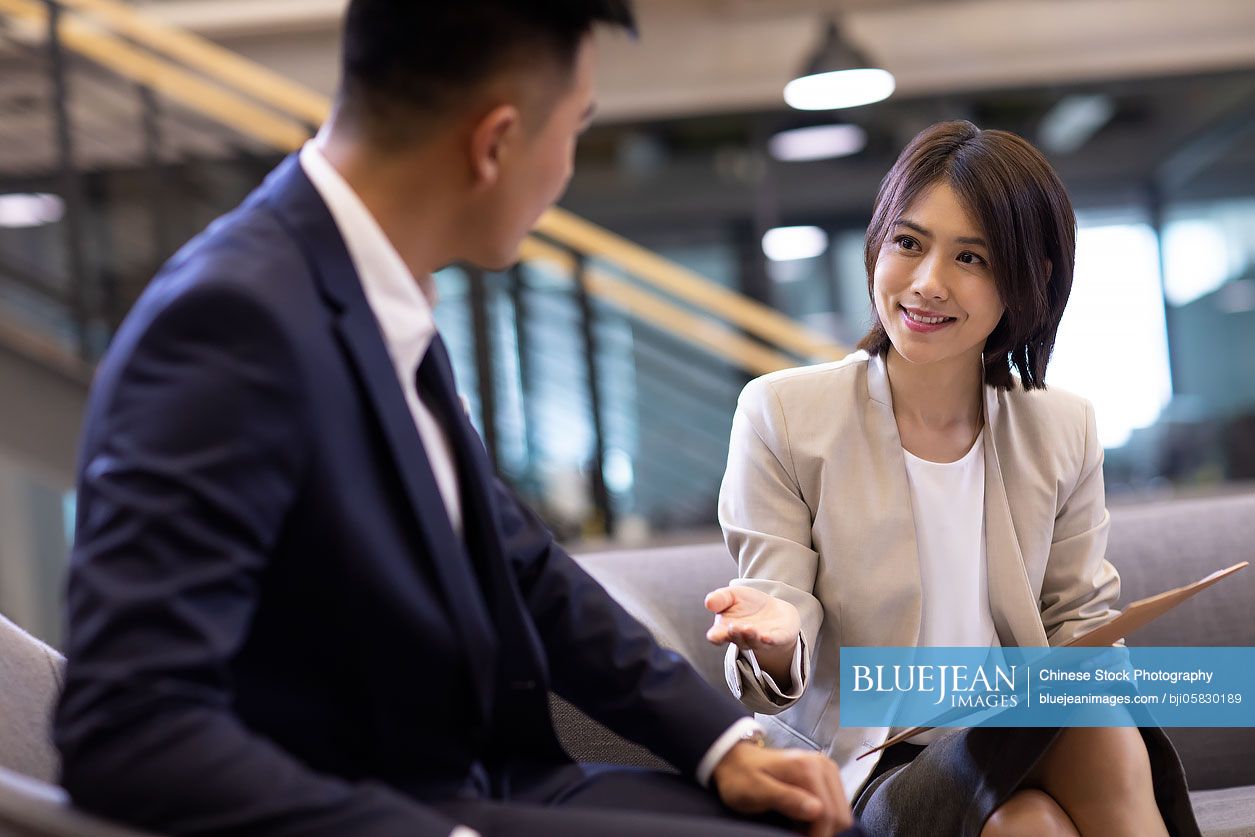 Young Chinese businesswoman and businessman talking in office 