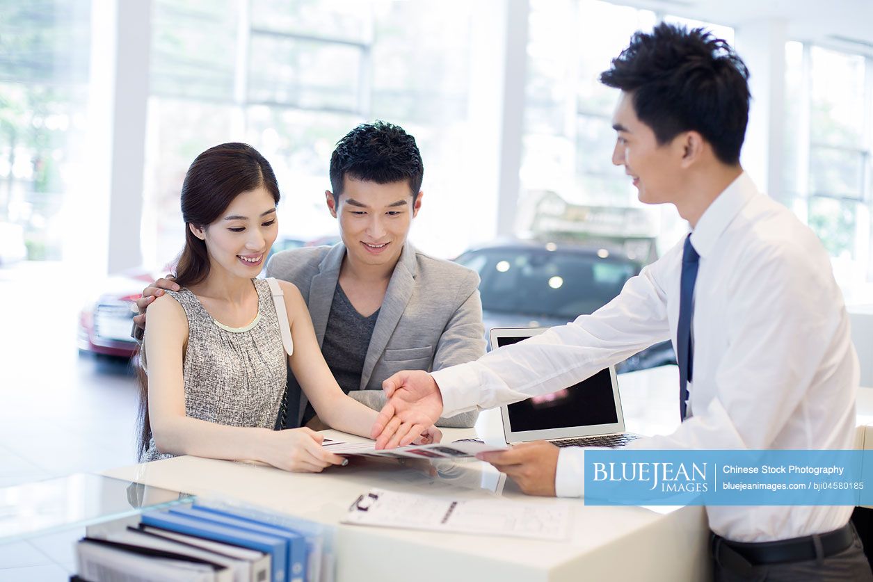 Young Chinese couple buying car in showroom