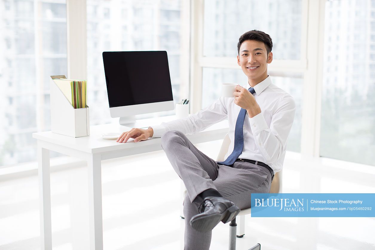 Cheerful young Chinese businessman taking a coffee break