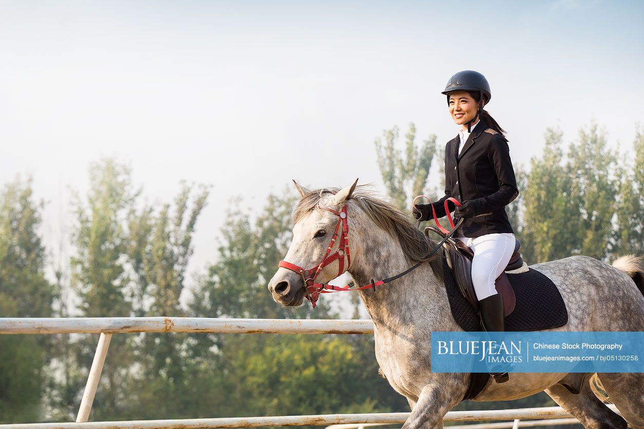 Cheerful young Chinese woman riding horse