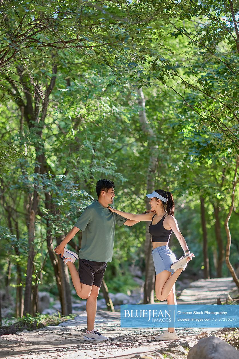 Young couple exercising outdoors, surrounded by a dense canopy of trees