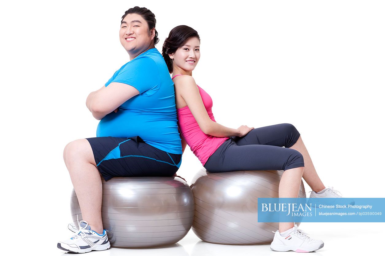 Chubby Chinese man and girlfriend sitting back to back on fitness balls