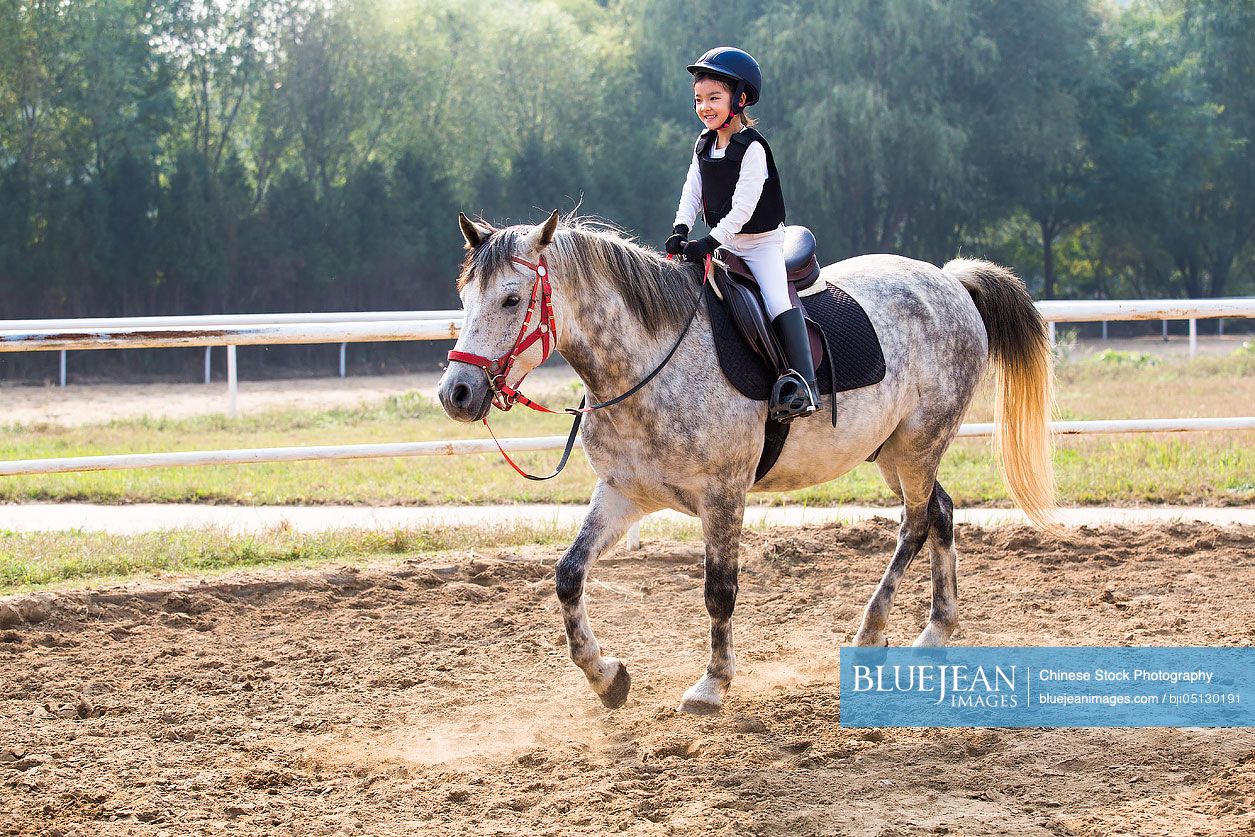 Cheerful little Chinese girl riding horse