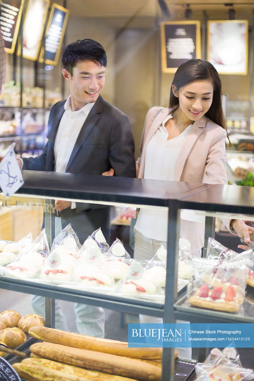 Young Chinese couple choosing cakes in bakery