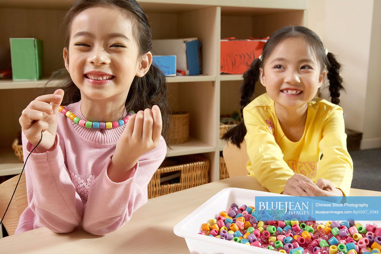 Chinese Girls Sitting In Classroom Smiling And Playing With Beads