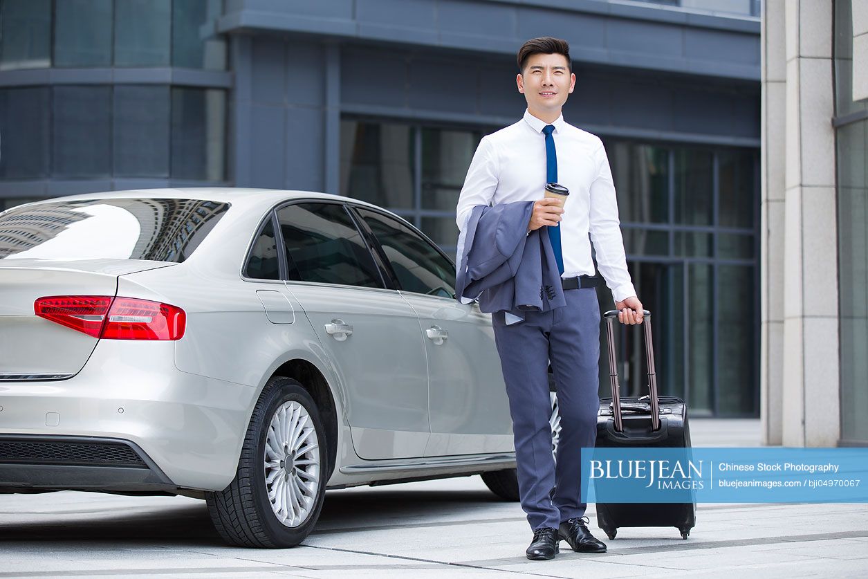 Confident Chinese businessman walking with wheeled luggage