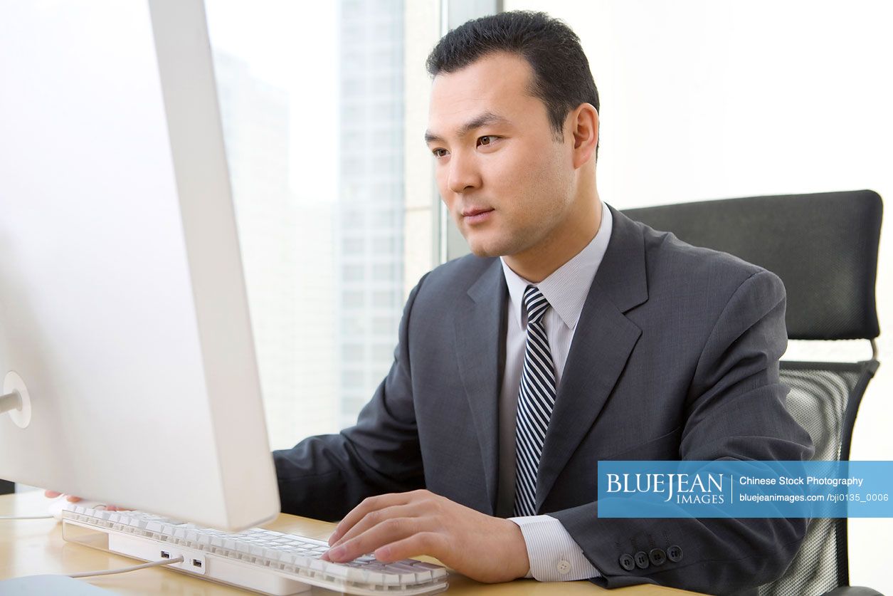 Chinese man uses computer in a well-lit, sunny office