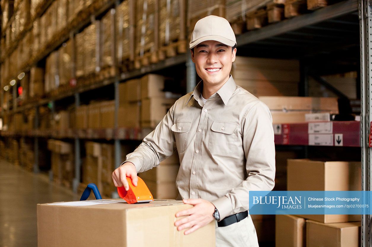 Male Chinese warehouse worker packing a box