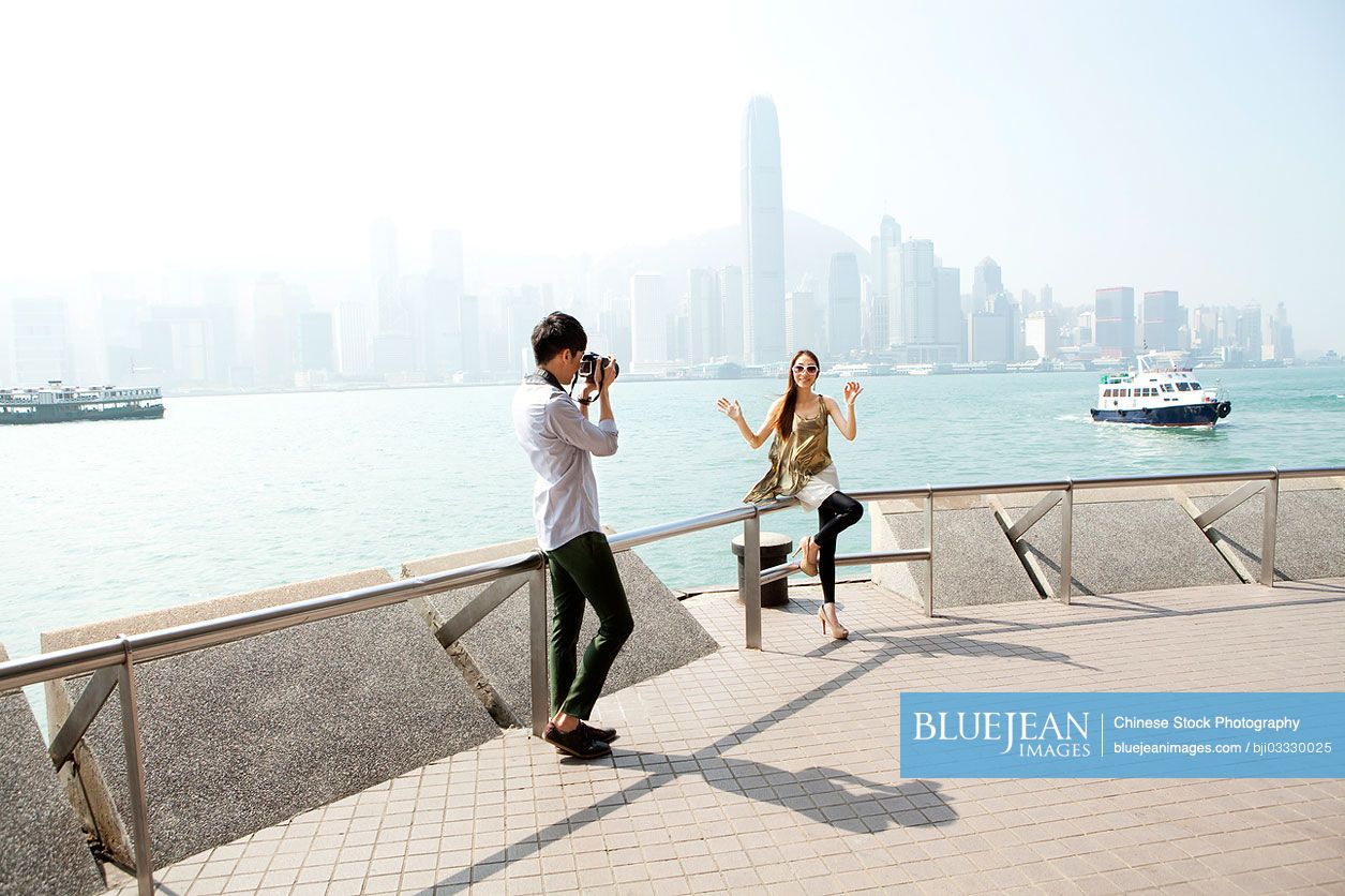 Happy young Chinese man photographing young women with SLR camera in Victoria Harbor, Hong Kong