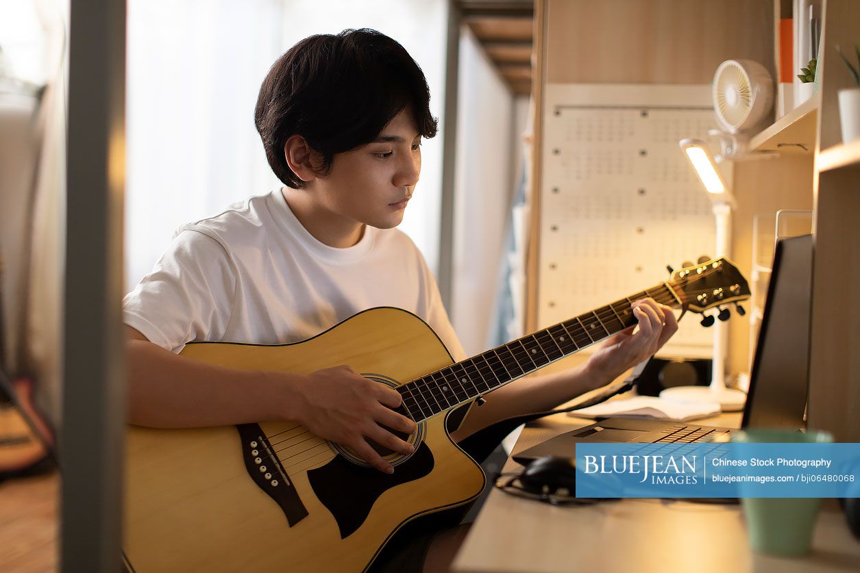 Young Chinese university student playing guitar in dormitory