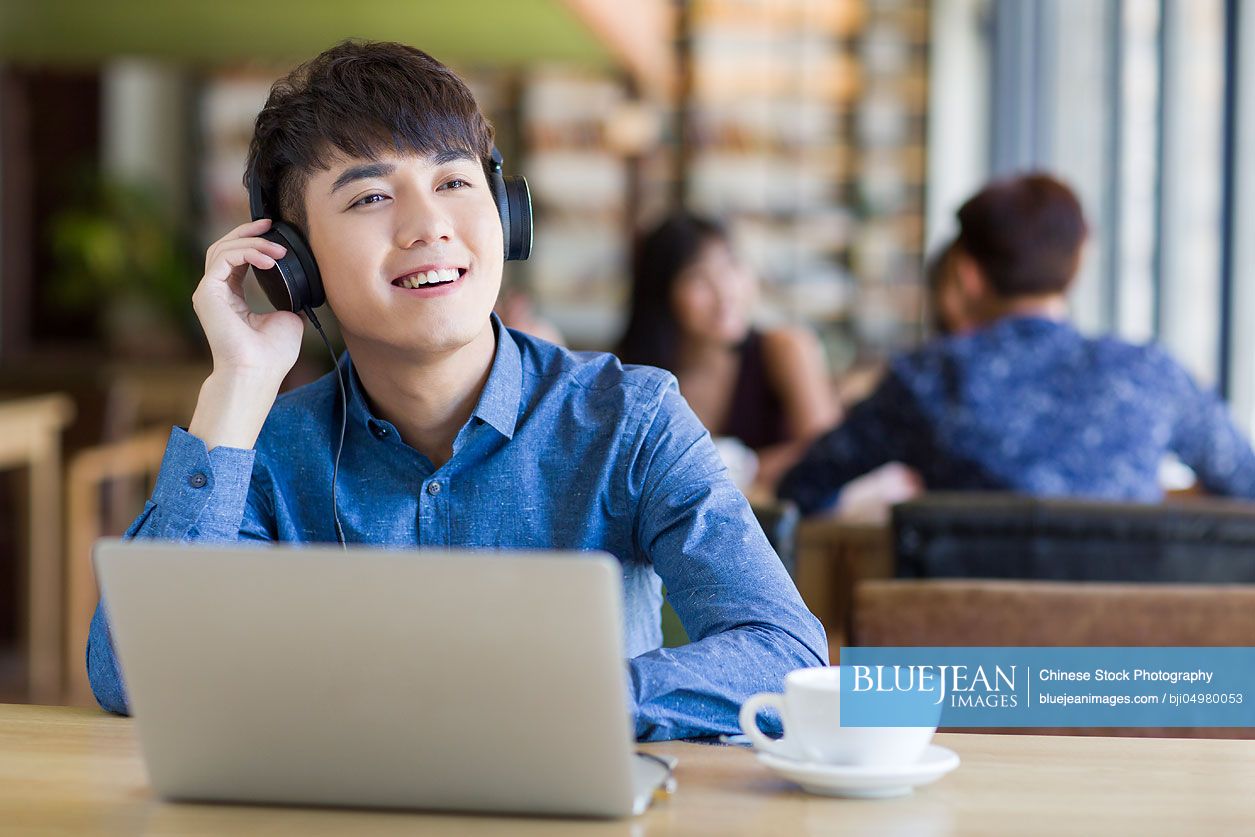 Young Chinese man listening to music in café