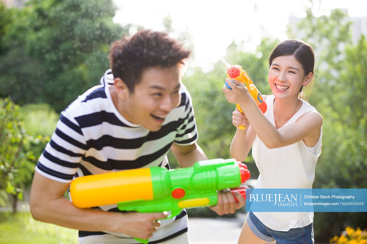 Happy young Chinese couple playing squirt guns